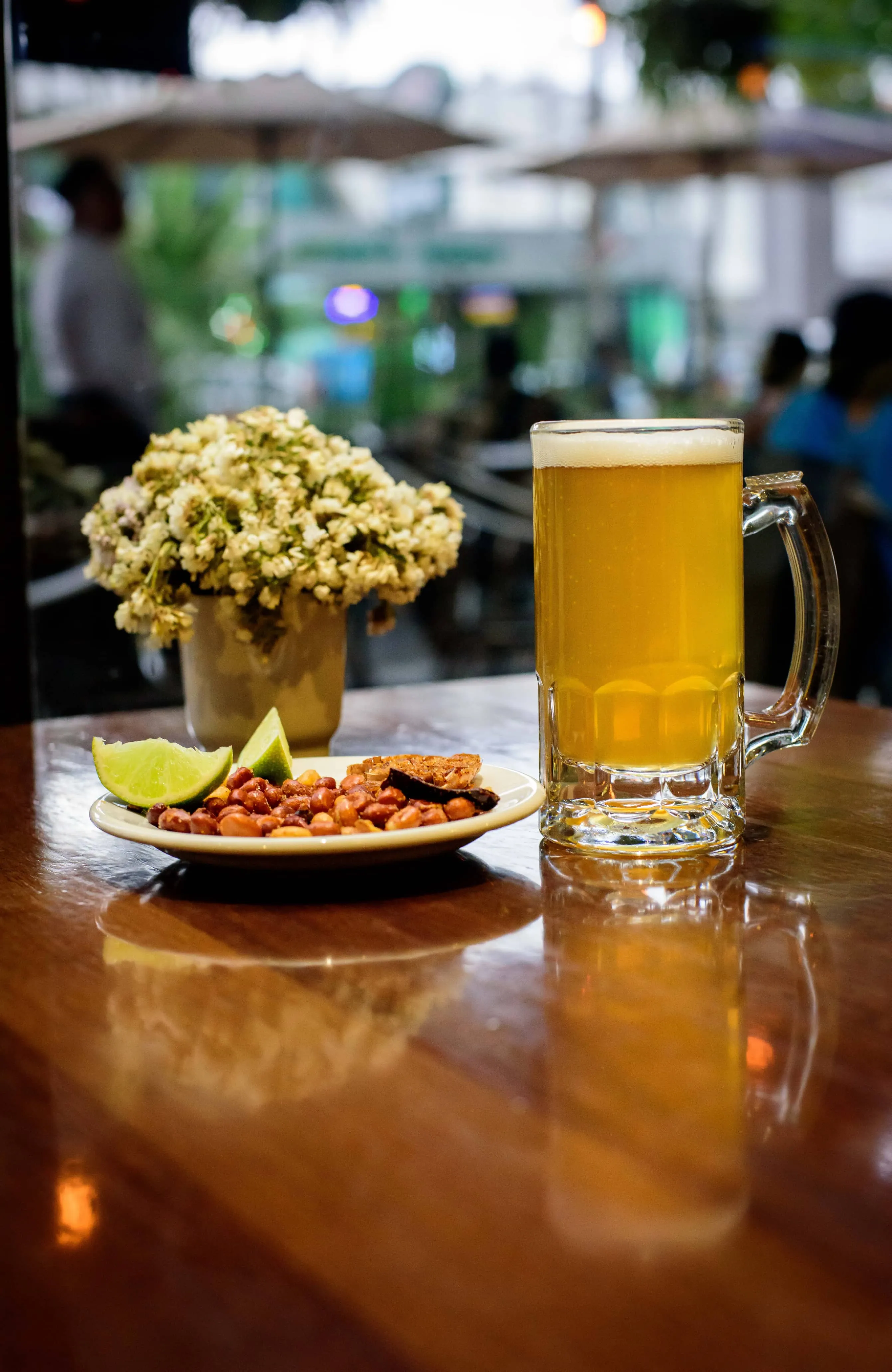 Sucursal Del Jardín - Plaza Parque  con una  cerveza unos cacahuates y al fondo se pueden ver mesas con gente fuera de foco
